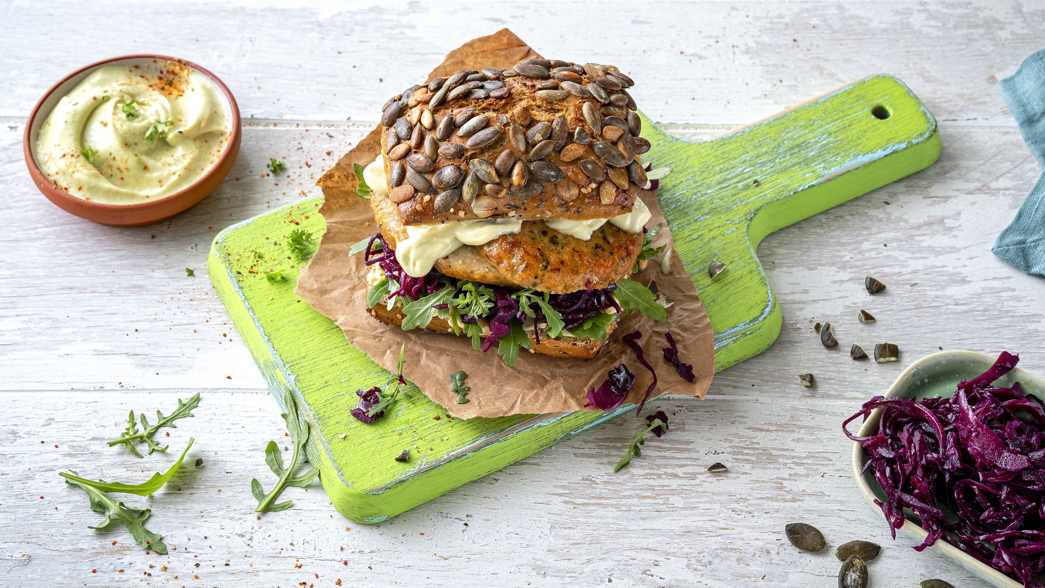 Belegtes Brötchen mit Dip in Schale serviert auf grünem Holzbrett